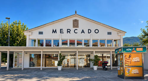 Edificio del mercado de Baiona con fachada blanca, amplios ventanales y entrada cubierta en planta baja