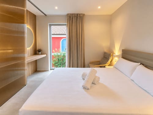 Dormitorio moderno en apartamento Holibai de Baiona con cama blanca, iluminación cálida, detalles de madera y acceso a terraza