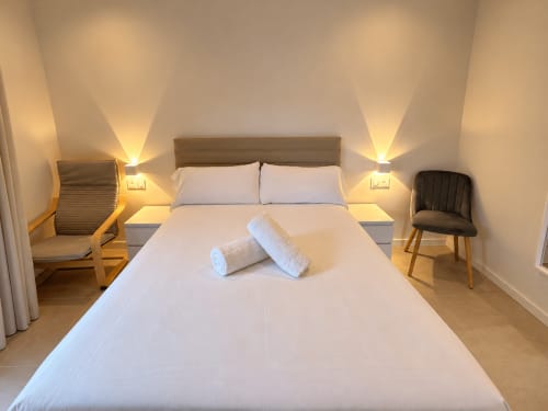 Dormitorio moderno del apartamento Holibai en Baiona con cama doble, ropa de cama blanca, lámparas de noche y muebles de madera