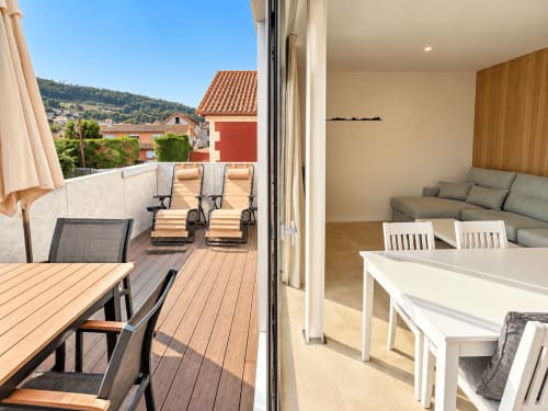 Terraza del apartamento Holibai en Baiona con tumbonas, zona de comedor y vistas a la ciudad con edificios de tejado rojo