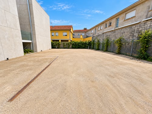 Amplio patio del apartamento Holibai en Baiona con edificio moderno, casa amarilla y muros de piedra bajo cielo azul