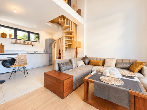 Moderno apartamento diáfano en Douvaine con escalera de caracol de madera, sofá gris, cocina y comedor con vistas al lago