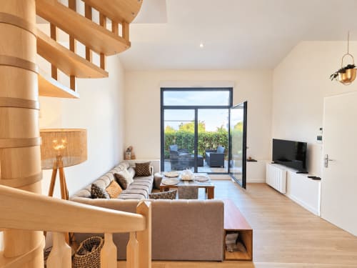 Salón moderno diáfano con escalera de caracol, sofá beige, muebles de madera y puertas de cristal que abren a la terraza