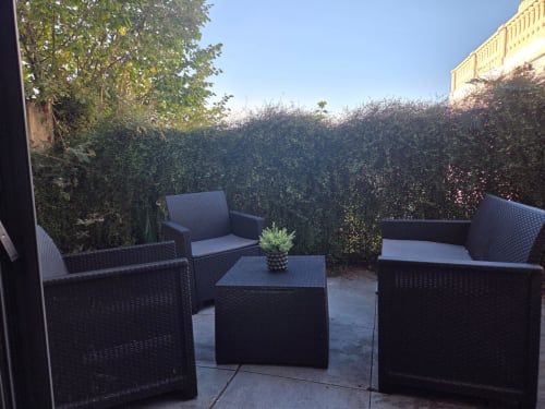 Área de descanso exterior con muebles de ratán negro, cojines y plantas en maceta, rodeada de setos cubiertos de hiedra en el hotel NN Patrimoine