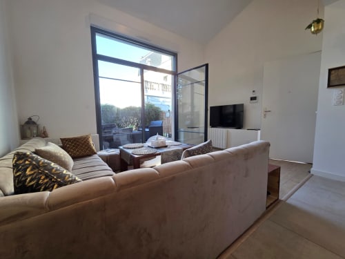 Sala de estar moderna del apartamento La Perla del Leman, hotel Douvane, con sofá beige, televisor de pantalla plana y vista al lago Leman