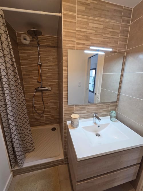 Baño moderno en NN Patrimoine Douvaine con lavabo blanco, ducha con azulejos de madera, espejo e iluminación LED