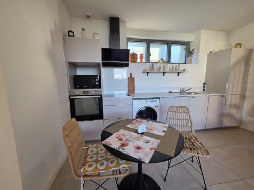 Cocina moderna y comedor en el apartamento La Perle du Léman, Douvaine, con muebles blancos, sillas tejidas y vistas al lago