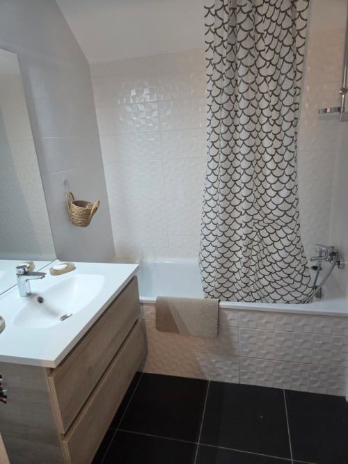 Baño moderno en el apartamento La Perle du Léman, Douvaine, con azulejos blancos, tocador de madera, cortina de ducha con patrón de escamas y