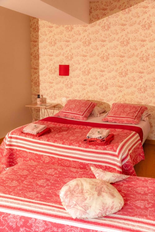 Charming bedroom at Moulin de Gaubourg B&B with red and cream toile wallpaper, coordinating bedding, and rustic nightstand.