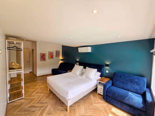 Modern bedroom at Vindihouses B&B in Epinac with queen bed, blue accent wall, sofa, and wooden flooring.