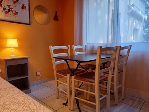 Coin repas Suite Shangaï de la Royal Palmeraie, Aubagne - chaises en bois, table noire, murs orange, lampe, vue sur le jardin