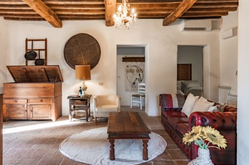 Salotto rustico toscano con travi in legno, divano rosso, girasoli e arredi d'epoca a Buonconvento