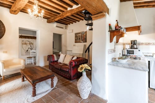 Rustico appartamento toscano a Buonconvento con travi in legno a vista, divano in pelle rossa e piccola cucina in marmo