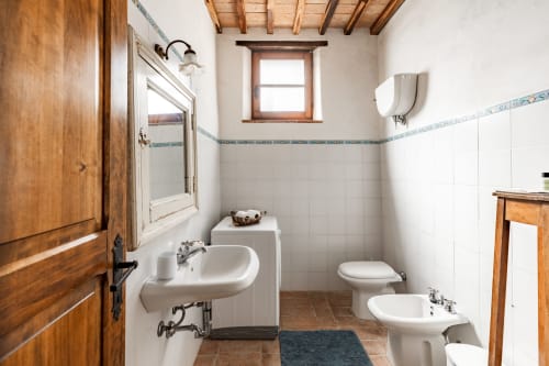 Bagno rustico italiano dell'hotel Buonconvento con piastrelle bianche, travi in legno, doppio lavabo e bidet