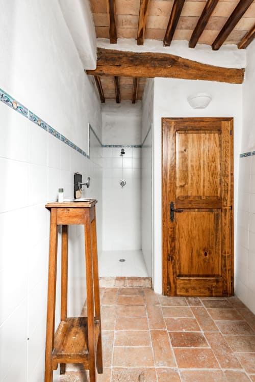 Bagno rustico con travi in legno, piastrelle in terracotta, lavabo in legno e porta nell'appartamento di Buonconvento