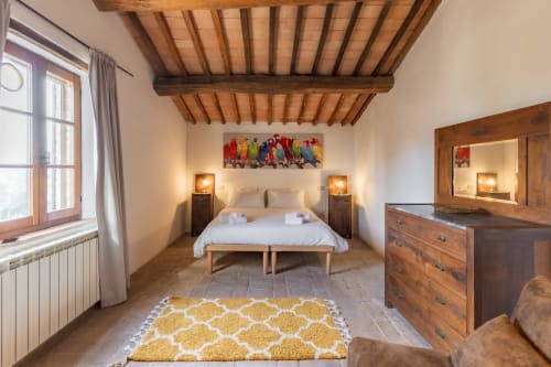 Spaziosa camera da letto all'hotel Quarantallina di Buonconvento con travi in legno a vista, letto bianco, mobili in legno e colori vivaci