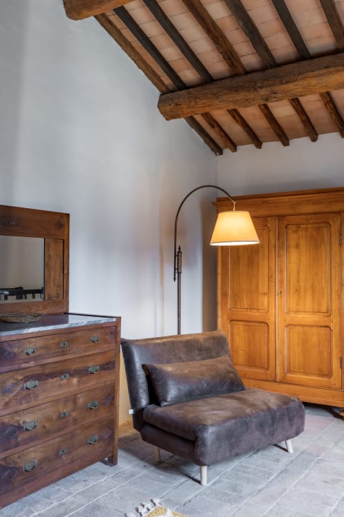 Camera rustica dell'hotel Quarantallina a Buonconvento con travi in legno a vista, poltrona in pelle scura, comò in legno