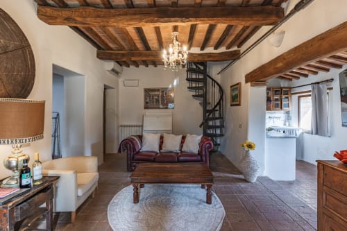Accogliente salotto dell'hotel Buonconvento con travi in legno a vista, divano bordeaux e scala a chiocciola