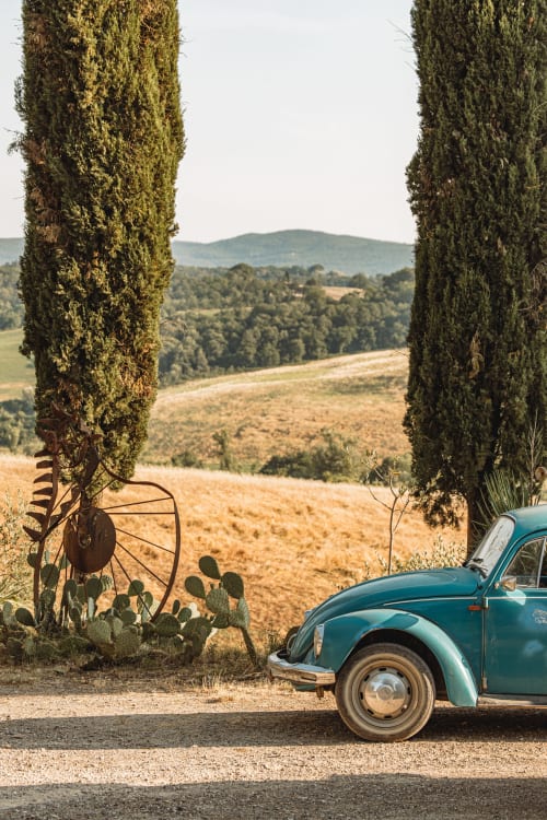 Auto vintage turchese parcheggiata tra i cipressi con vista sulle dolci colline della Toscana vicino a Buonconvento