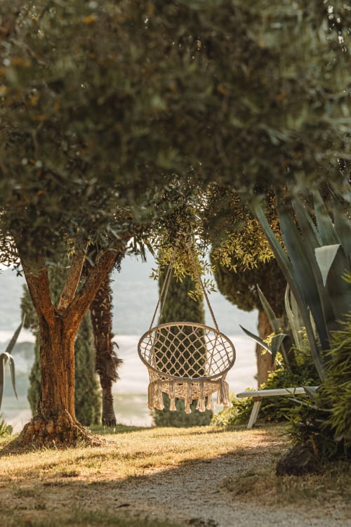 Sedia sospesa in macramé tra i cipressi dell'hotel Quarantallina a Buonconvento, Italia