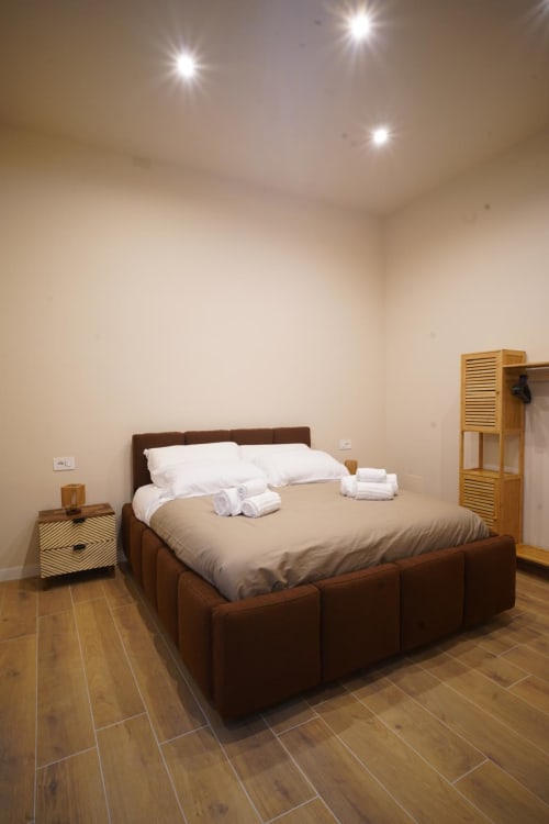 Camera San Severo dell'hotel Domusè di Napoli con letto marrone, cuscini bianchi, comodino in legno e faretti a incasso