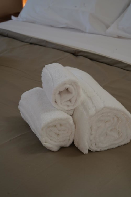 Tre asciugamani bianchi arrotolati sul pavimento in piastrelle beige della camera San Severo dell'hotel Domusè a Napoli