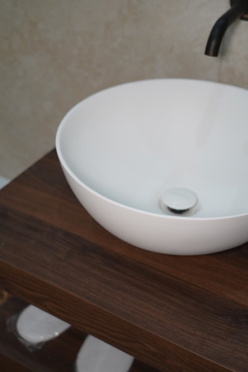 Moderno lavabo rotondo bianco su mobile in legno scuro presso l'hotel Domusè di Napoli, con rubinetteria nera e parete beige