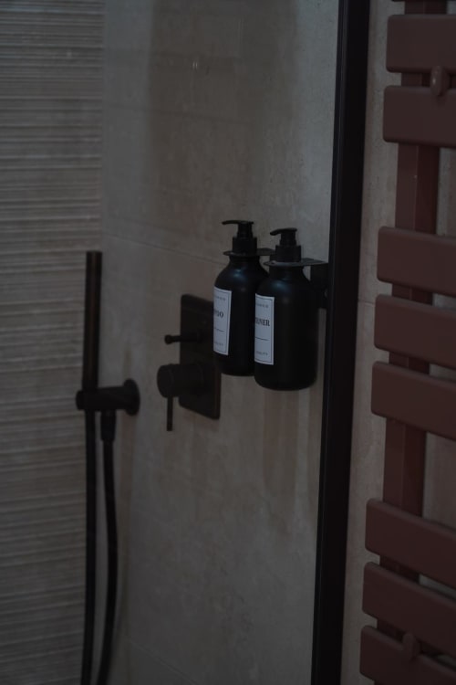 Dispenser neri per il bagno montati su parete beige nella camera Capodimonte dell'hotel Domusè, Napoli