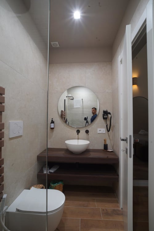 Moderno bagno della camera Domusè Capodimonte, Napoli con specchio rotondo, lavabo bianco e vanity in legno scuro