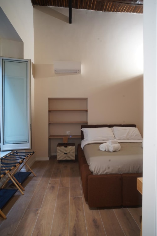 Camera Capodimonte dell'hotel Domusè a Napoli con letto biancheria bianca, scaffali in legno, condizionatore e servizi moderni
