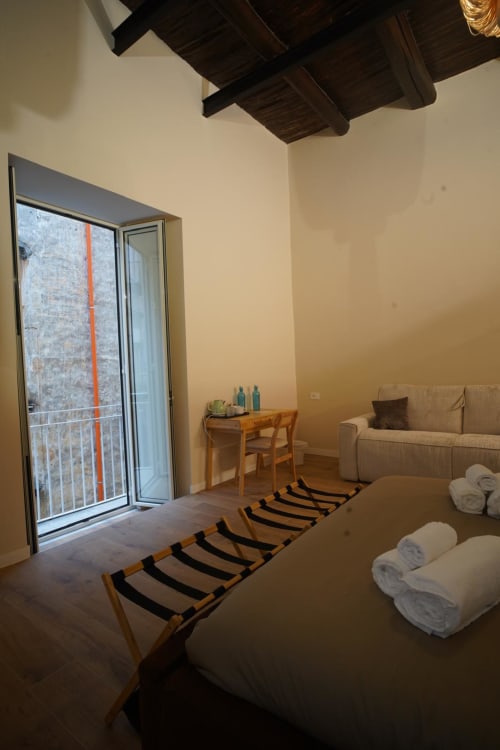 Camera San Gennaro presso Domusè Napoli con letto, balcone, divano, scrivania in legno e travi a vista