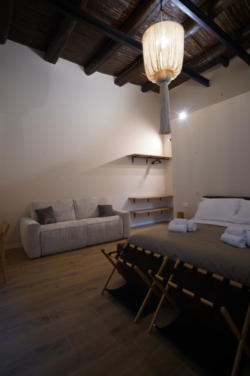 Camera San Gennaro a Domusè hotel Napoli: moderna camera da letto con divano, letto, lampada a sospensione e travi in legno