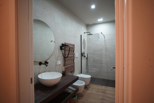 Bagno moderno dell'hotel Domusè a Napoli con specchio rotondo, lavabo da appoggio, doccia walk-in e finiture in legno