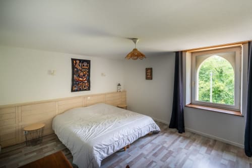 Chambre lumineuse au Domaine des Escouanes avec tête de lit en bois, literie blanche, fenêtre cintrée et parquet