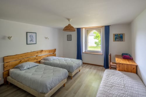Chambre d'hôtes lumineuse avec lits en bois, fenêtre cintrée et décor rustique au Domaine Des Escouanes