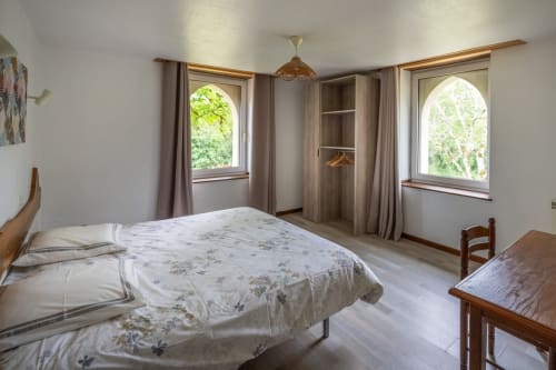 Chambre lumineuse au Domaine Des Escouanes avec lit queen-size, fenêtres cintrées, armoire en bois et décor rustique à Prudhomat
