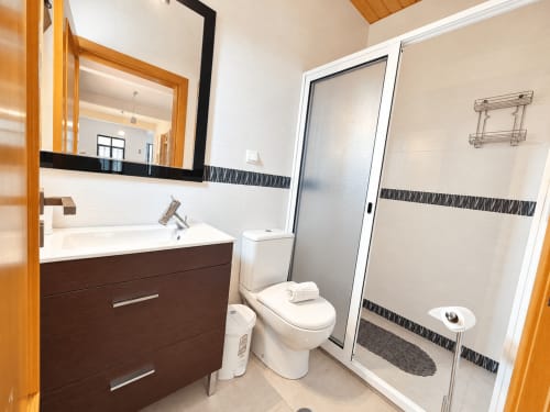 Modern bathroom in Casa do Moinho villa, Ribeira Brava, with dark wood vanity, white sink, toilet, and walk-in shower with
