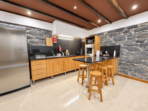 Modern kitchen with wooden cabinets, black countertops, stone walls, and bar seating at Casa do Moinho villa in Madeira.