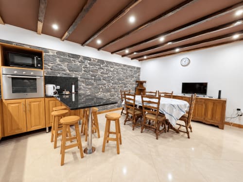 Modern villa living area with kitchen, dining table, wooden furniture, stone walls, beamed ceiling at Casa do Moinho, Madeira