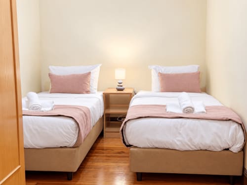 Twin beds in Casa do Moinho villa bedroom with white linens, pink accents, and wooden flooring
