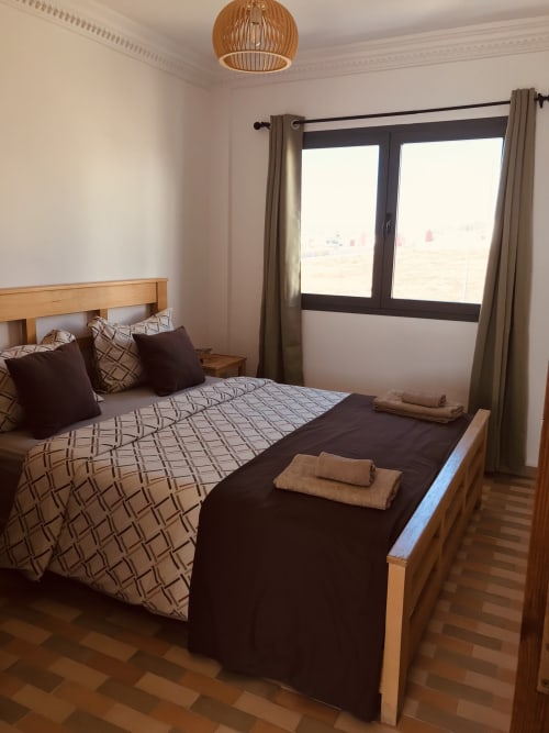 Bright bedroom at Imsouane Surf Paradise with wooden bed, sea view windows, and modern furnishings