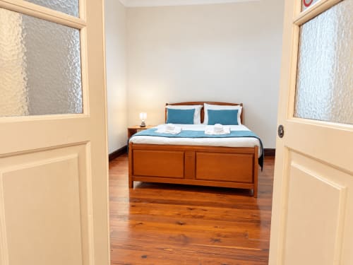 Bedroom at Casa do Moinho villa in Ribeira Brava with wooden bed, blue pillows, white linens, hardwood floors, and natural
