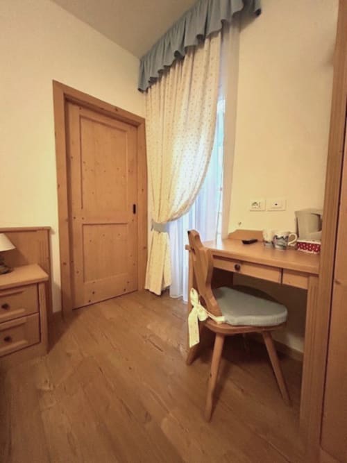 Genziana-Zimmer in der Residenza B&B Sissi in Almazzago mit Holzschreibtisch, Stuhl, Kleiderschrank und Vorhängen mit Stadtblick