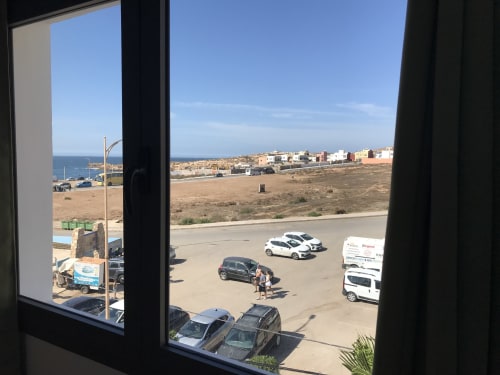 Sea view from Imsouane Surf Paradise hotel room overlooking beach, parking lot, and coastal town in Agadir, Morocco