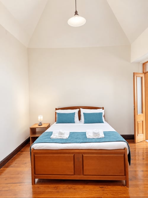 Bright bedroom at Check Madeira villa with wooden bed, blue linens, white sheets, nightstand, pendant light, and wooden door