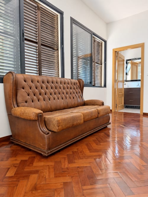 Brown leather tufted sofa in modern Check Madeira hotel suite with herringbone flooring and ensuite bathroom view