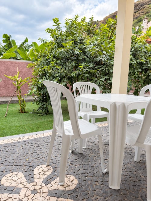White plastic outdoor furniture on paved patio with garden and hillside backdrop at Check Madeira, Ribeira Brava