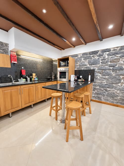 Modern kitchen at Check Madeira hotel in Ribeira Brava with wooden cabinets, dark counters, stone accent wall, and bar