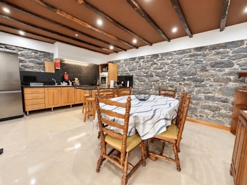 Open-plan kitchen and dining area with wood beams, stone walls, and rustic wooden table at Check Madeira, Ribeira Brava