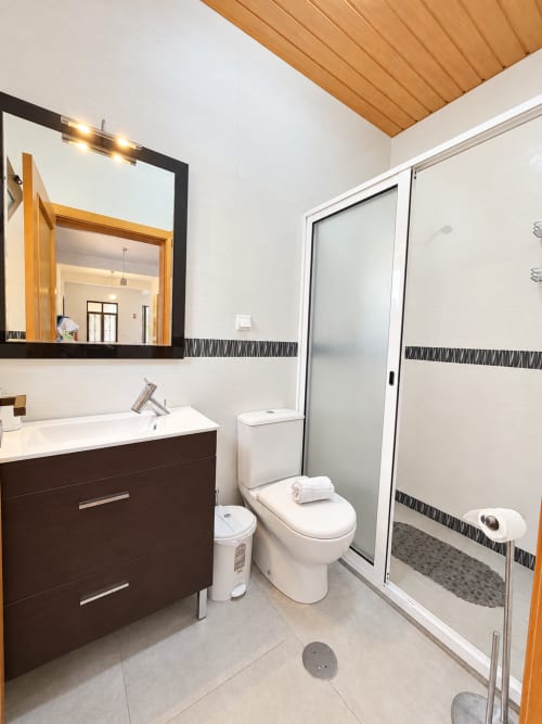 Modern bathroom at Check Madeira in Ribeira Brava with dark vanity, mirror, toilet, and walk-in shower with geometric tile
